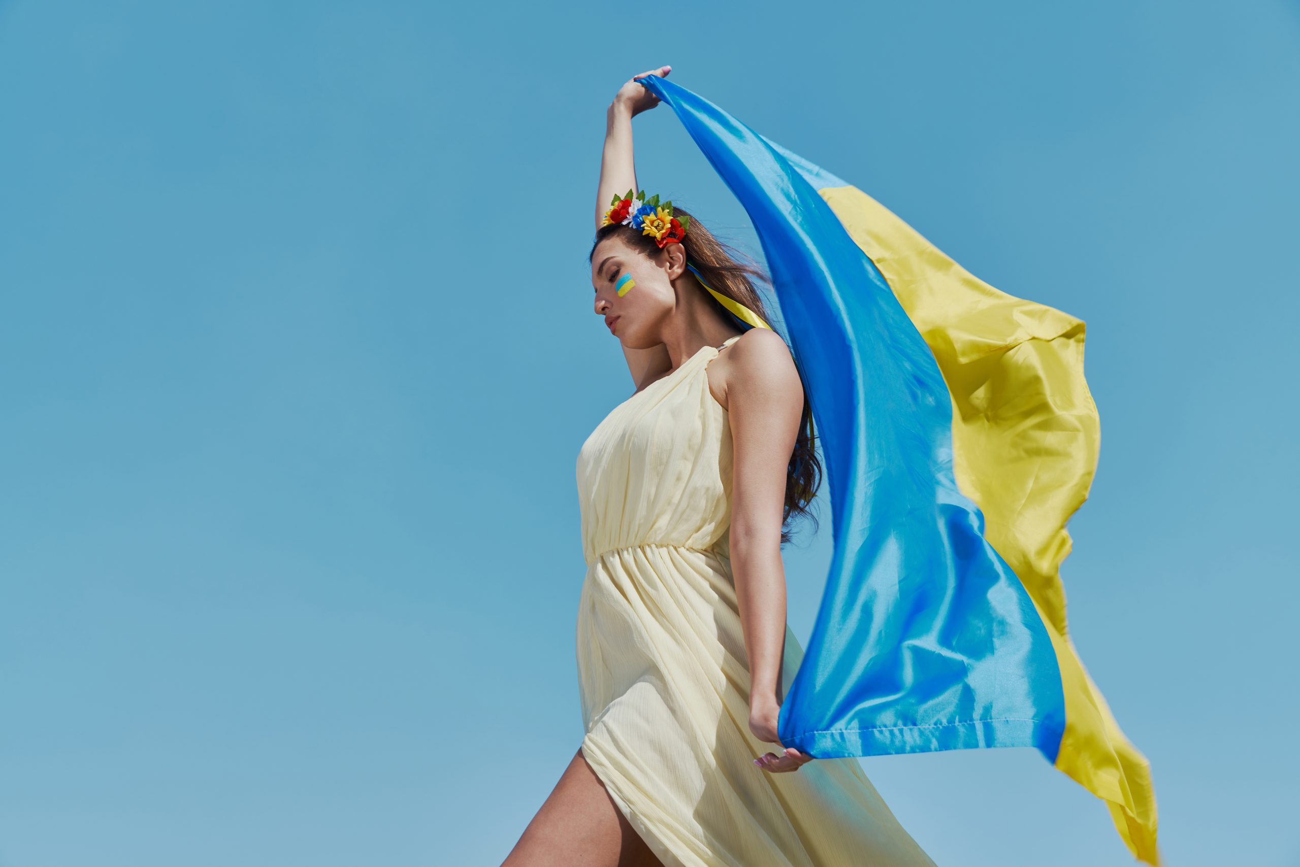 Attractive Ukrainian woman carrying national flag with sky in the background