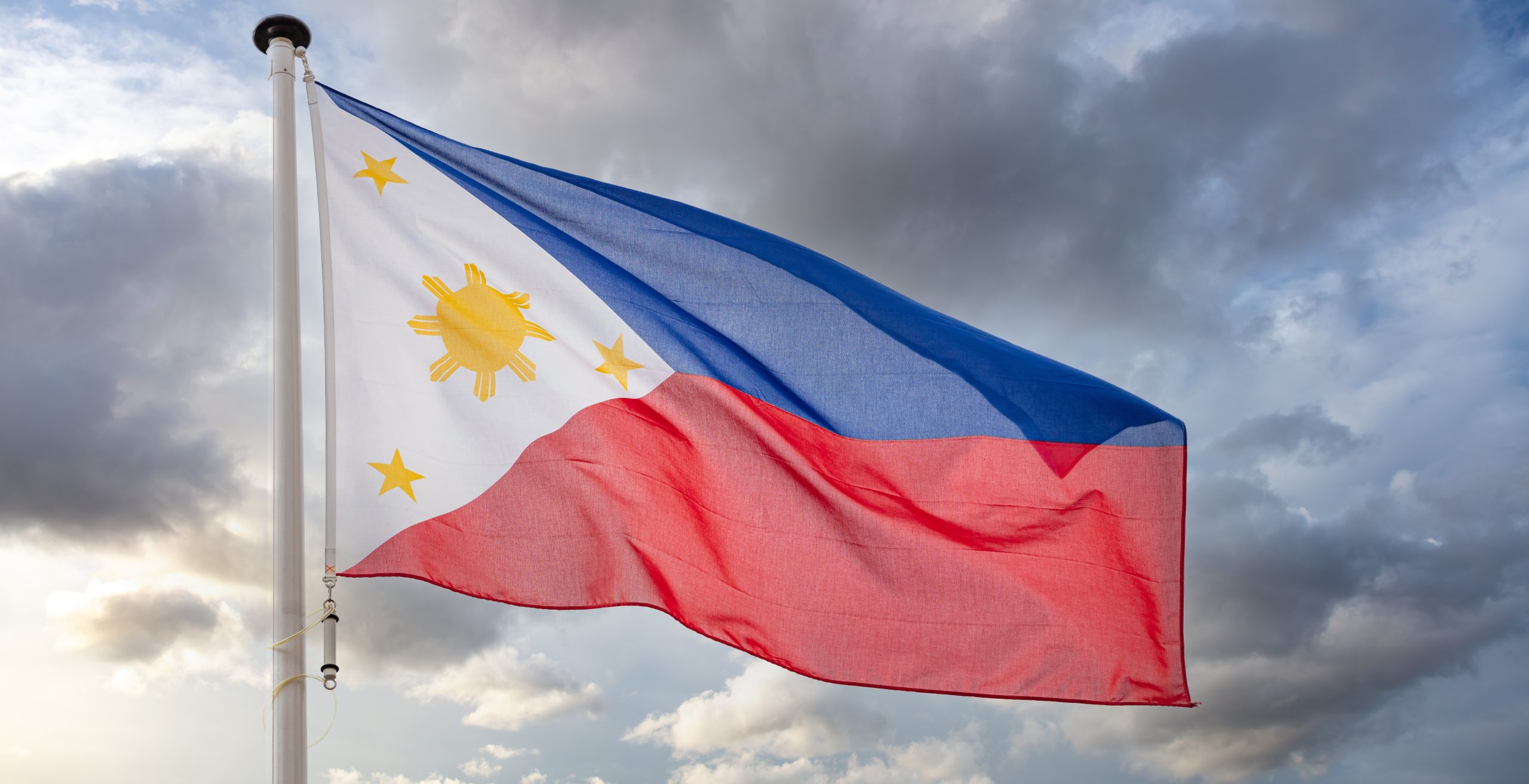 Philippines sign symbol. Republic of the Philippines national flag on a pole waving against cloudy sky background.