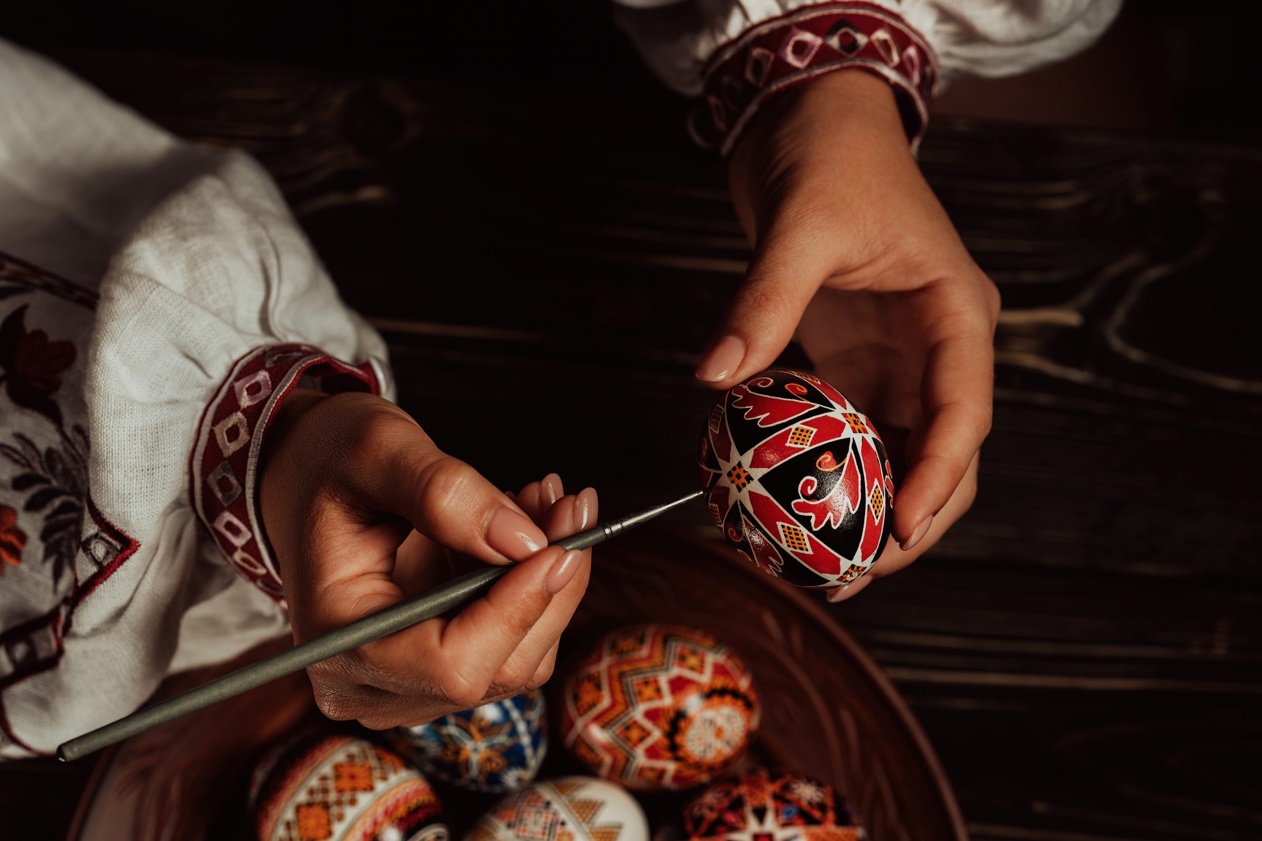 Ukrainian woman painting traditional ornamets on Easter egg - pysanka. Artist working in national costume. Preparation for Christian holiday.